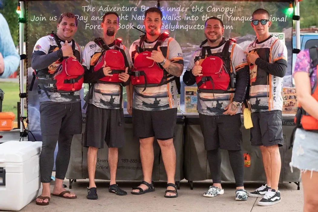 Five people posing with red life vests in front of a chalkboard wall and food counter