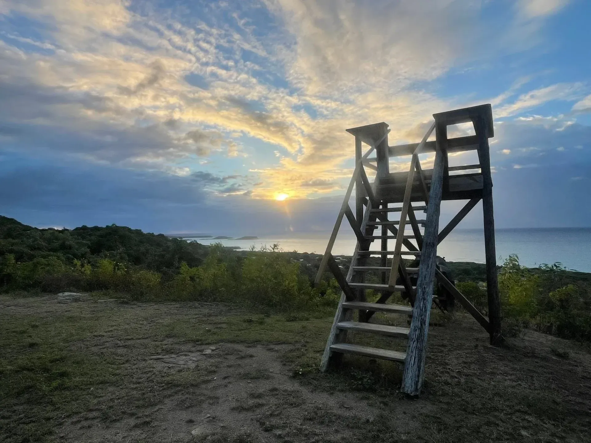 Wooden lookout tower at sunset on a grassy coastal overlook with dramatic clouds