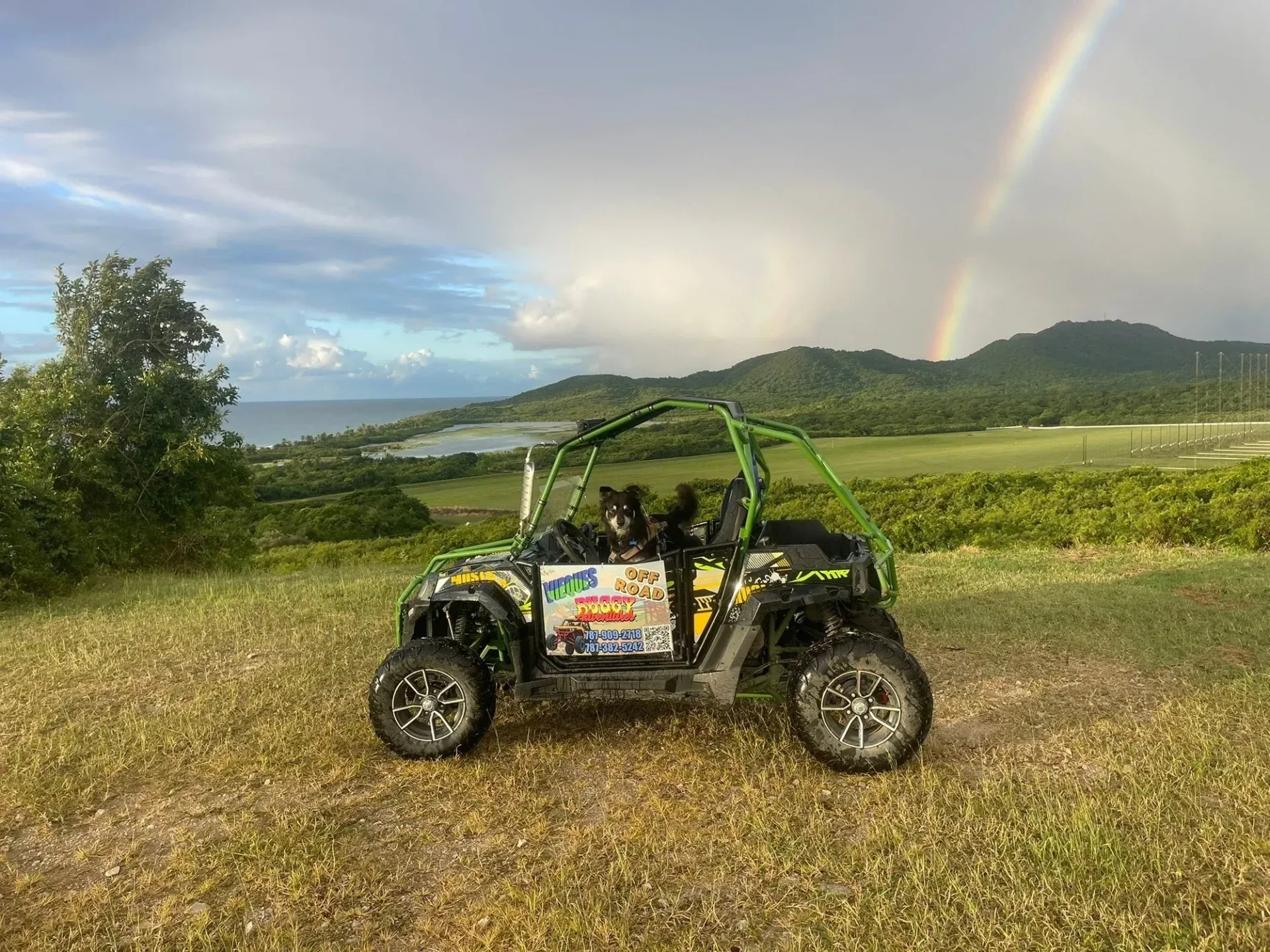 Off-road buggy parked on a grassy hill with rainbow and mountain view in the background