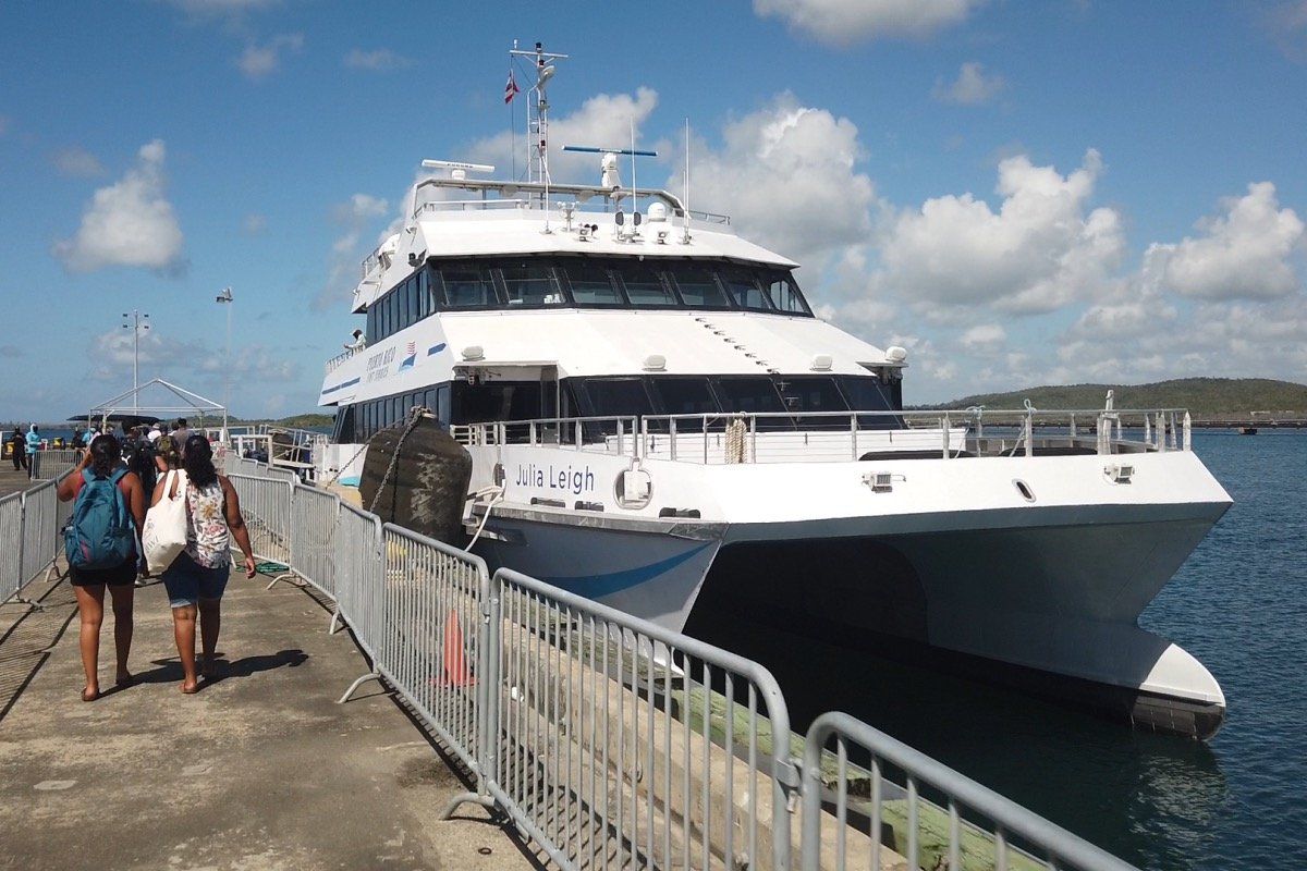 Large white ferry docked at a pier, with a few people walking beside it under a partly cloudy sky