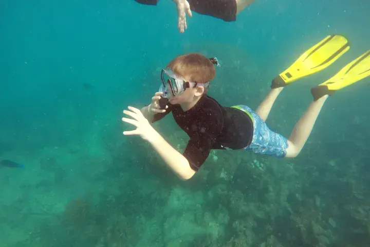 Snorkeler in black shirt and blue shorts swims underwater with yellow fins in clear turquoise water