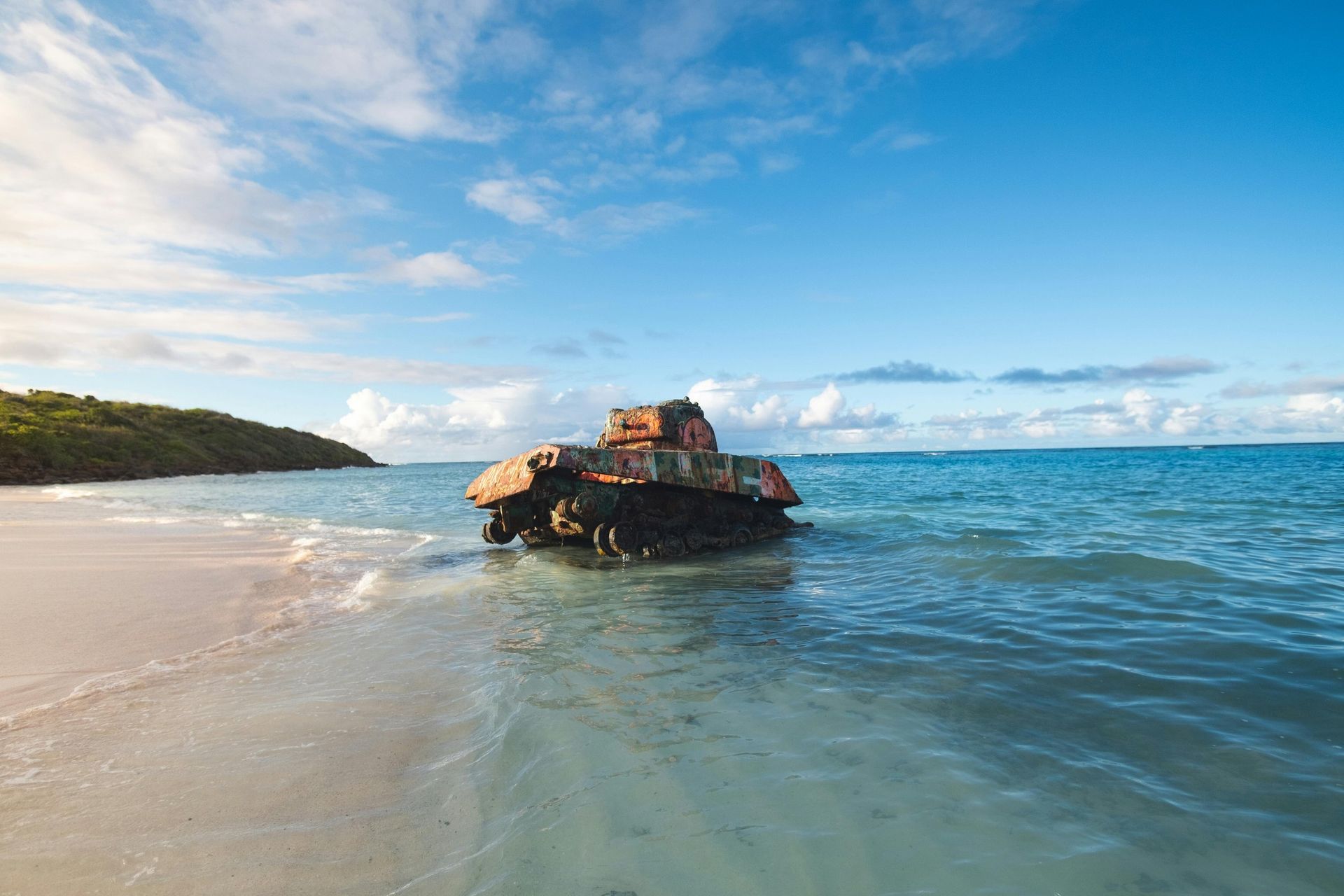 Rocky outcrop in a calm blue sea beside a sandy beach under a bright sky