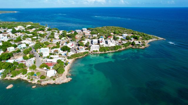 Aerial view of a coastal town with white houses beside turquoise water and a deep blue ocean.