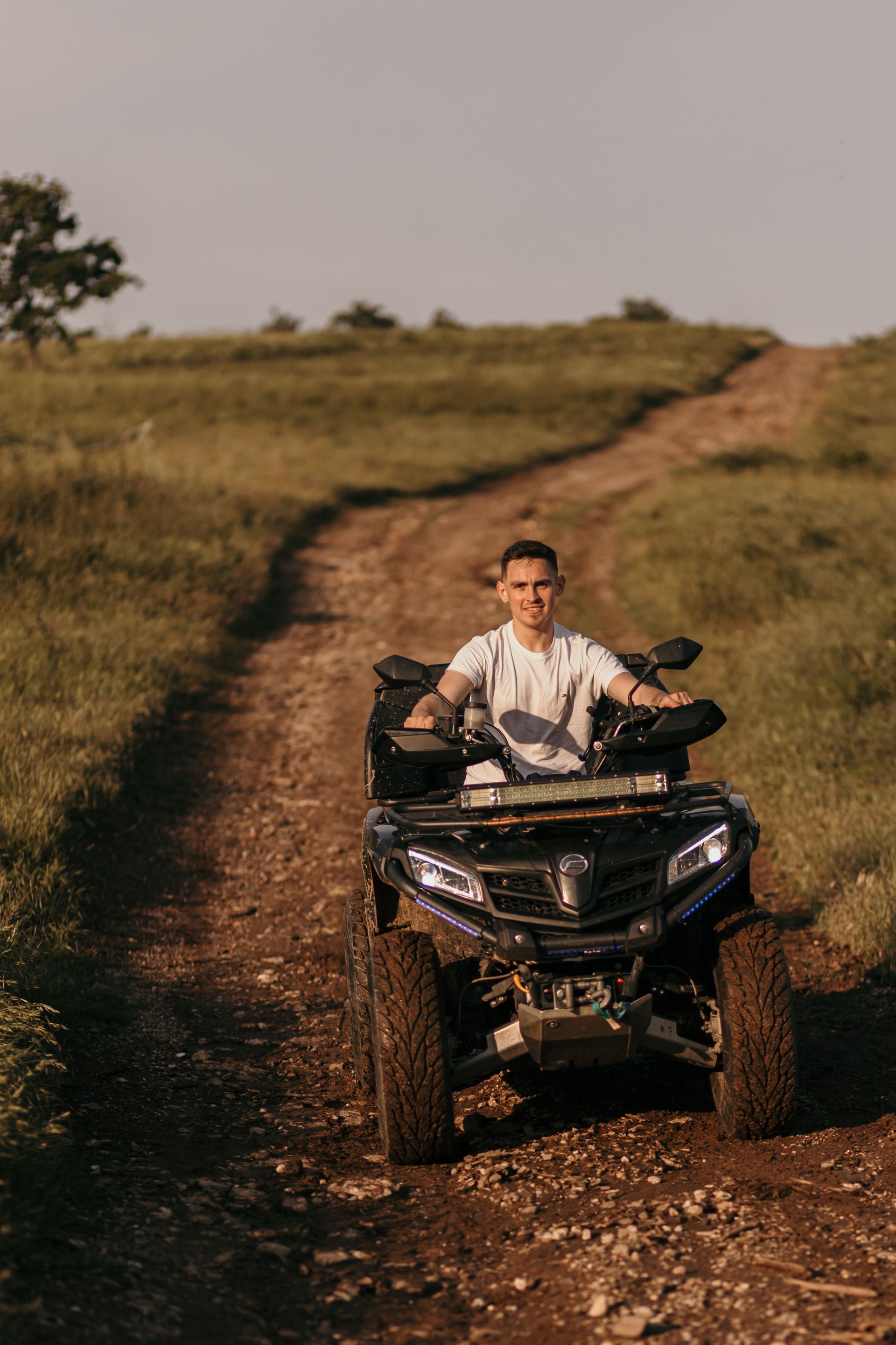Person riding an ATV on a dirt path through grassy hills