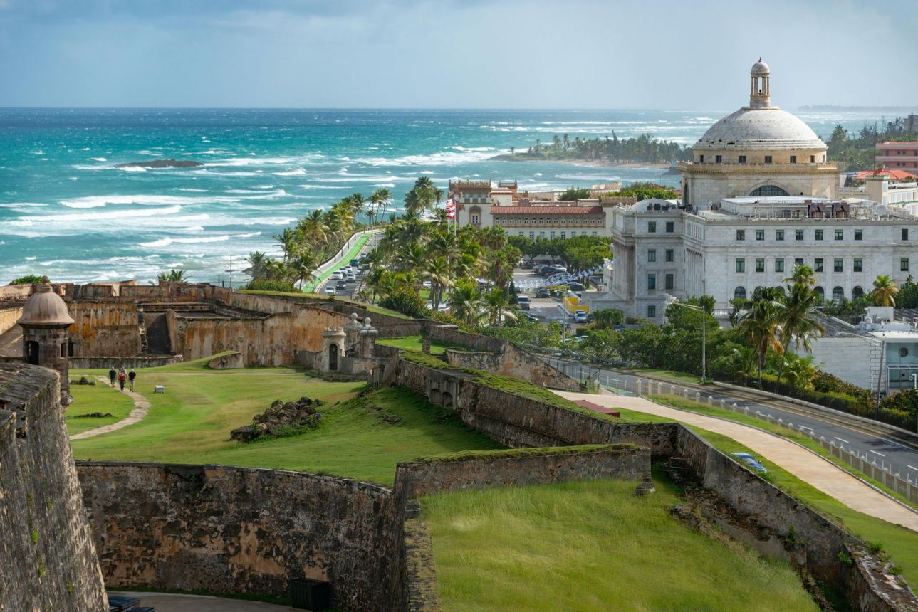 Historic stone fortress overlooking turquoise ocean and white domed building on a coastal hilltop