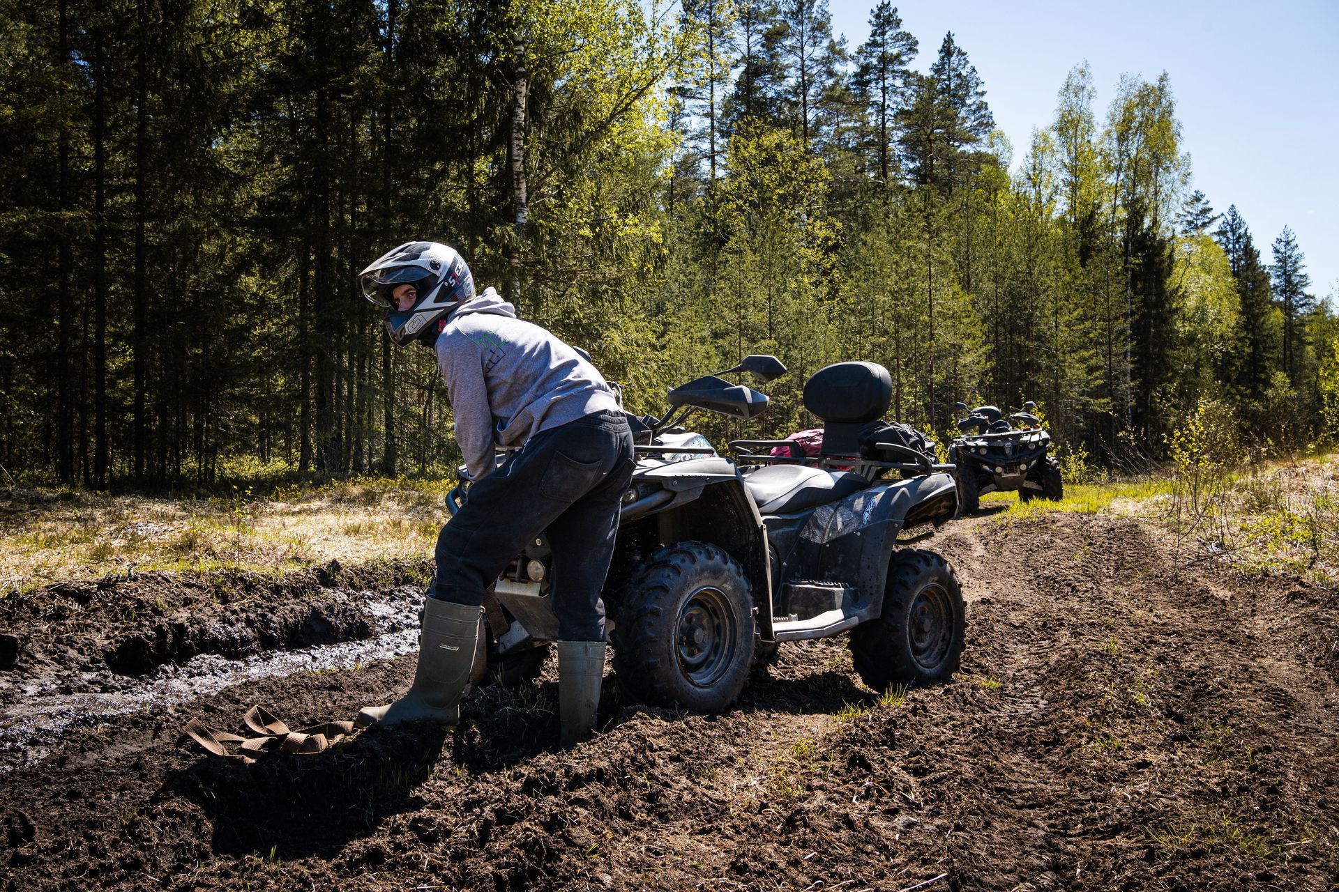 Person on an ATV in a muddy forest clearing, surrounded by trees and sunlight