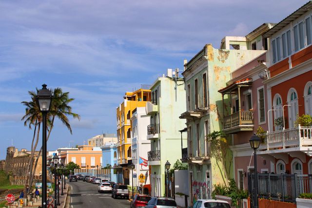 Sunlit colorful buildings lining a coastal street with palm trees and a blue sky