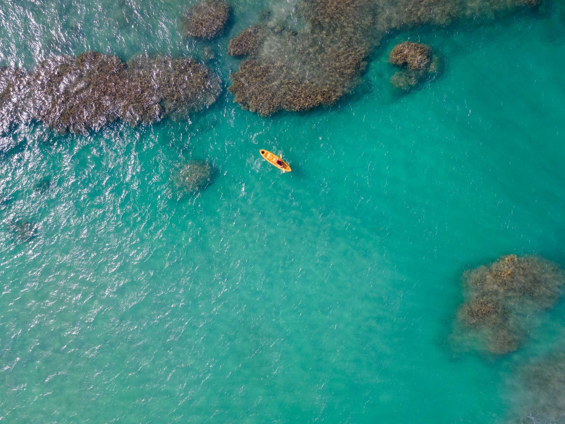 Orange kayak on turquoise water near dark rocky reef.