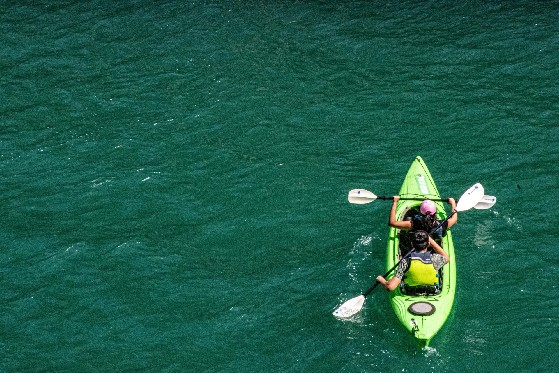 Single kayaker paddling a bright green kayak on teal water, viewed from above