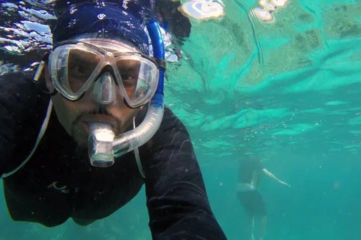 Snorkeler in black wetsuit and mask swimming underwater in clear turquoise water