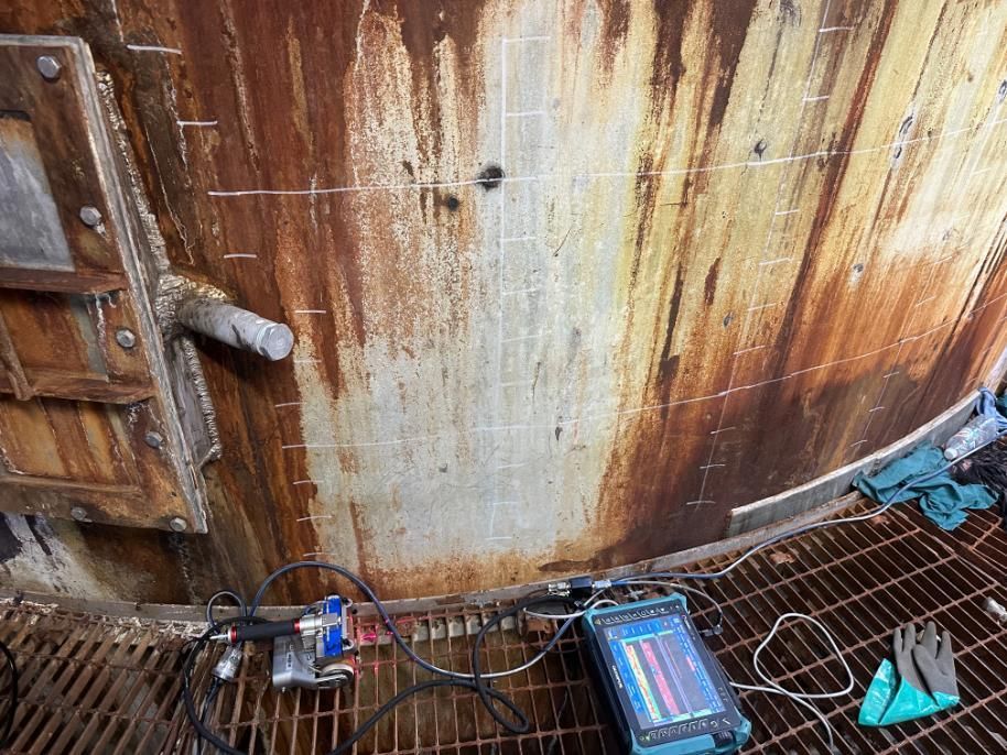 A Machine Is Sitting On A Metal Grate Next To A Rusty Wall — LJ's Technical Services In Burdell, QLD