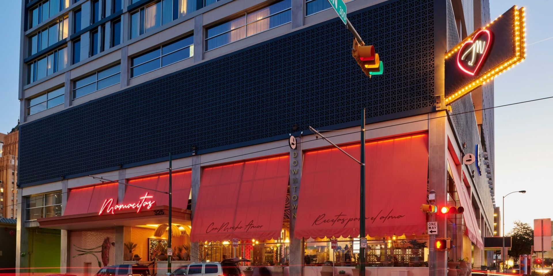 Exterior of a tall building with a red awning over a restaurant, and a lit-up neon sign.