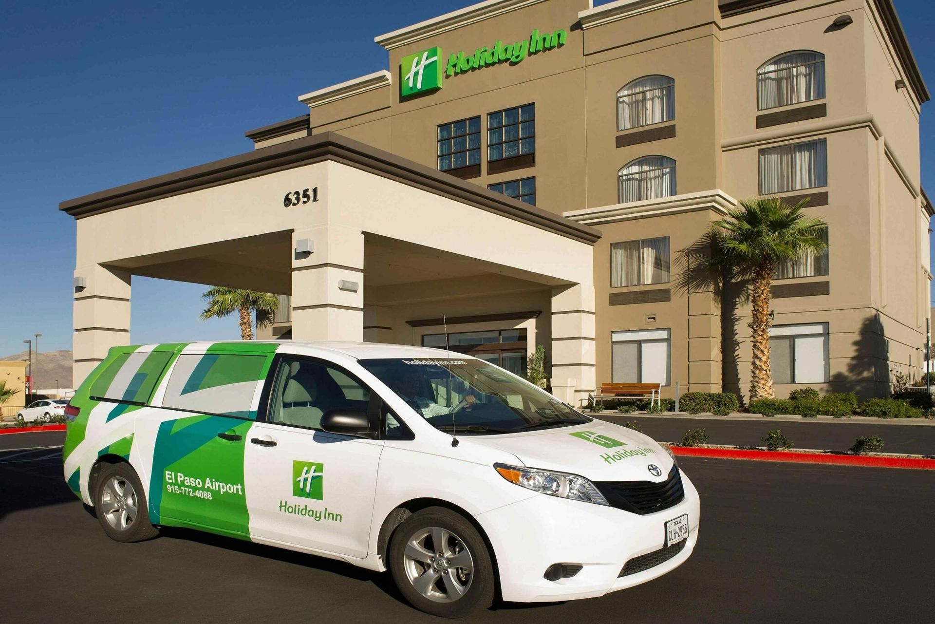 A white Holiday Inn shuttle van parked in front of the hotel with a green and white logo.