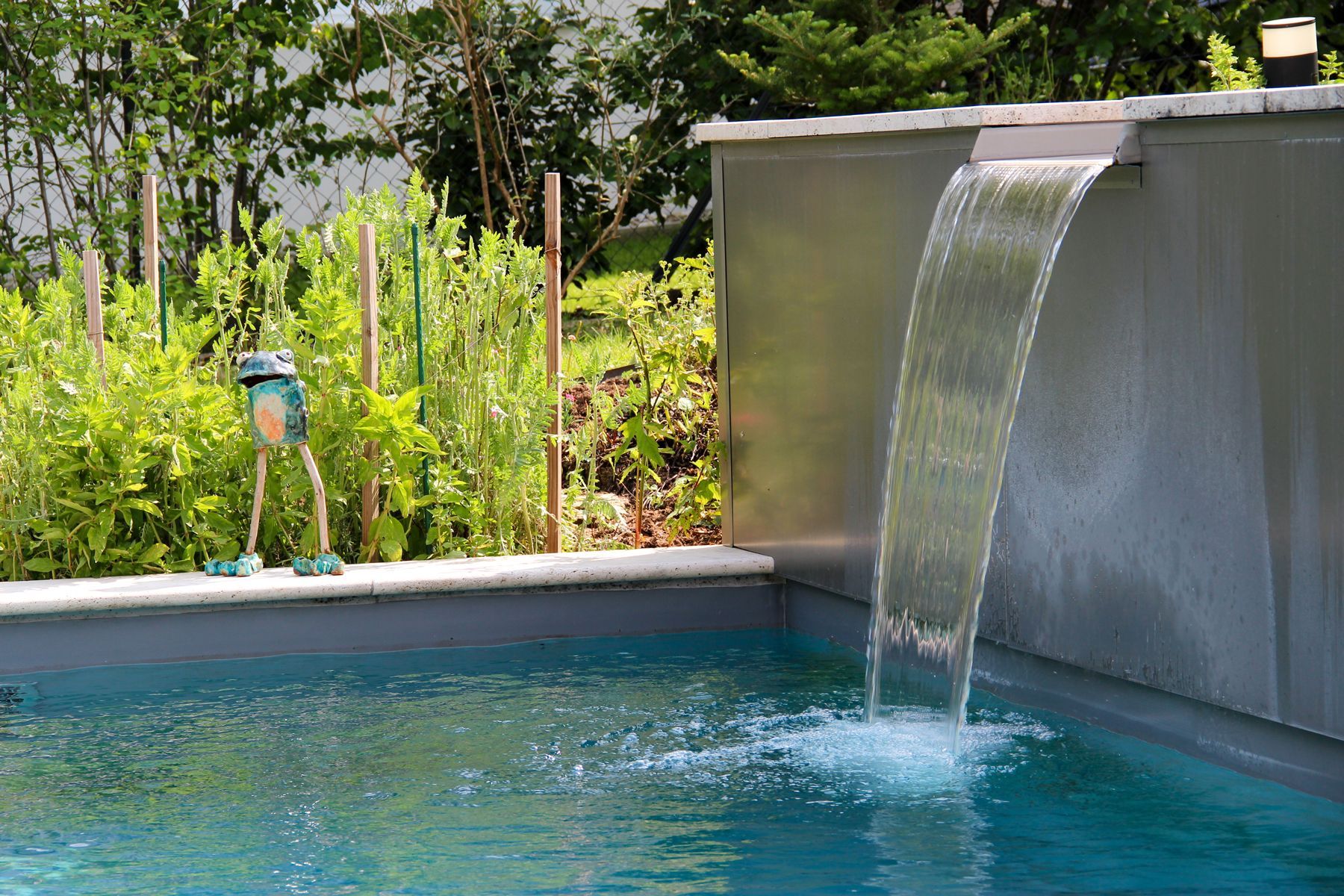 Hinterhofpool mit Wasserfallfunktion und im Hintergrund eine Person, die Pflanzen pflegt.
