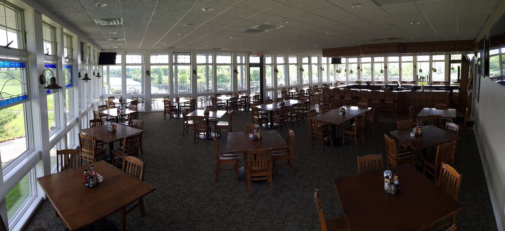 Restaurant interior with tables and chairs, large windows, and a dark carpet.