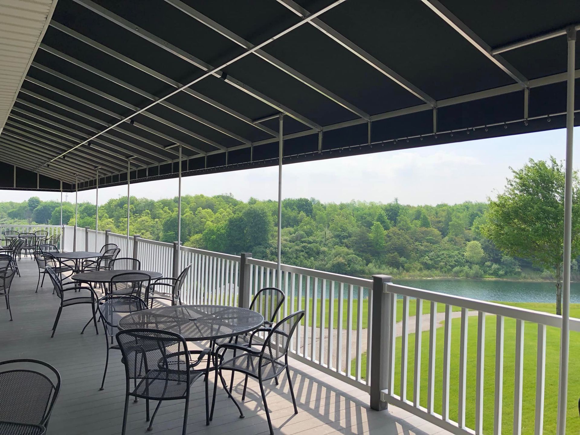 Covered outdoor patio with tables and chairs overlooking a green landscape and water.