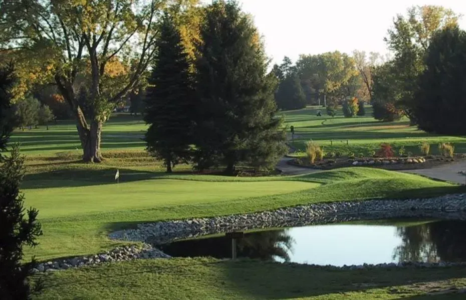 Golf green with pond and trees. Bright sunlight on course, fall foliage.