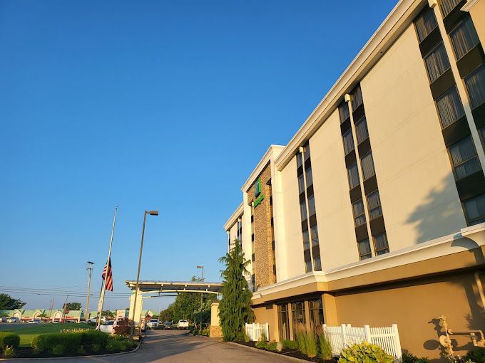 Hotel exterior under a clear blue sky. Beige and tan building with green accents, flag at half-mast.