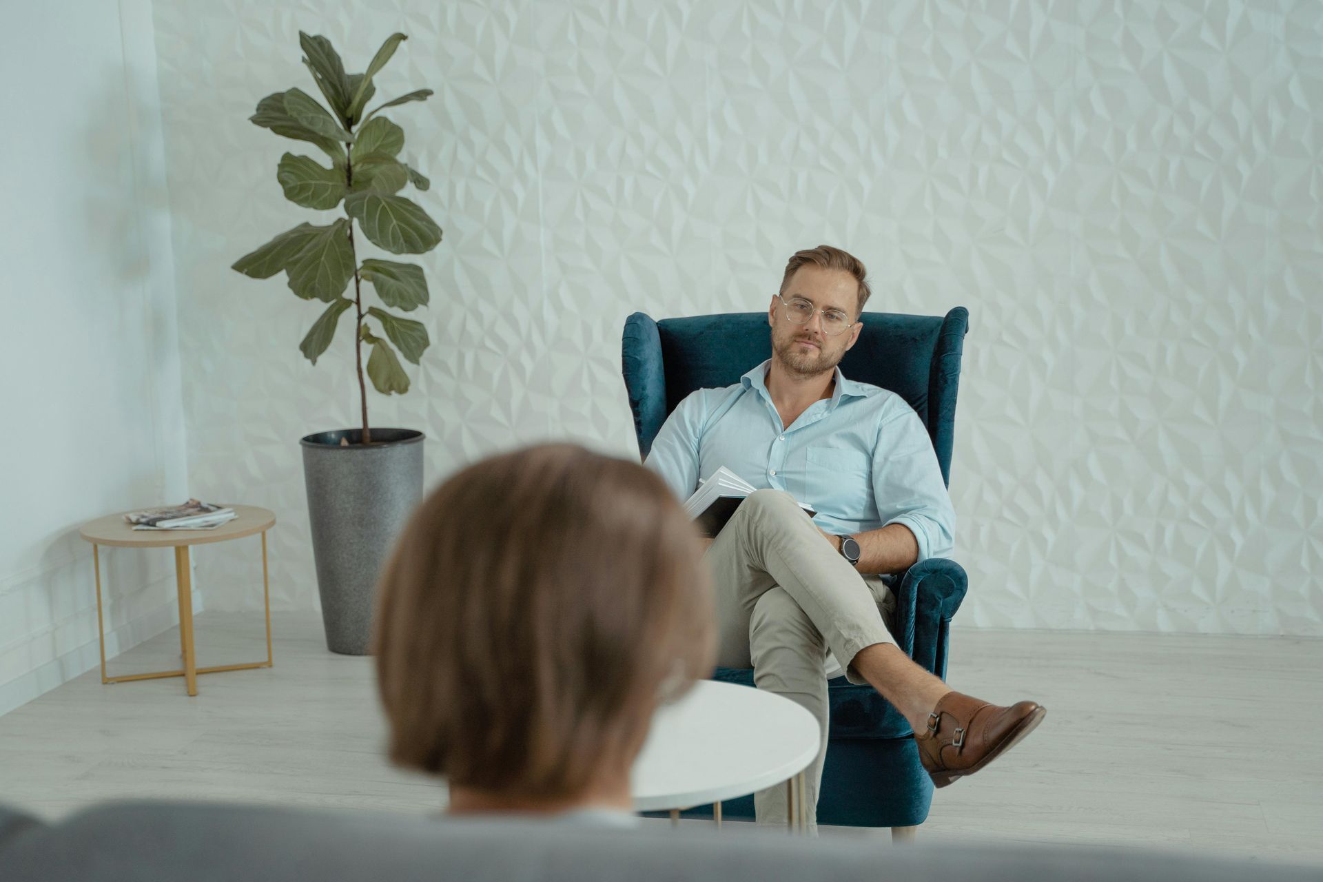 Coach in een blauwe fauteuil tegenover een patiënt in een spreekkamer.