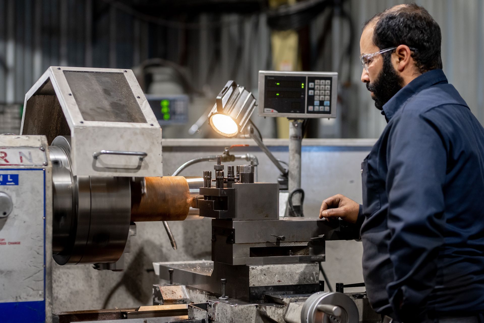 Homme opérant un tour dans un atelier, concentré, éclairé par une petite lampe.