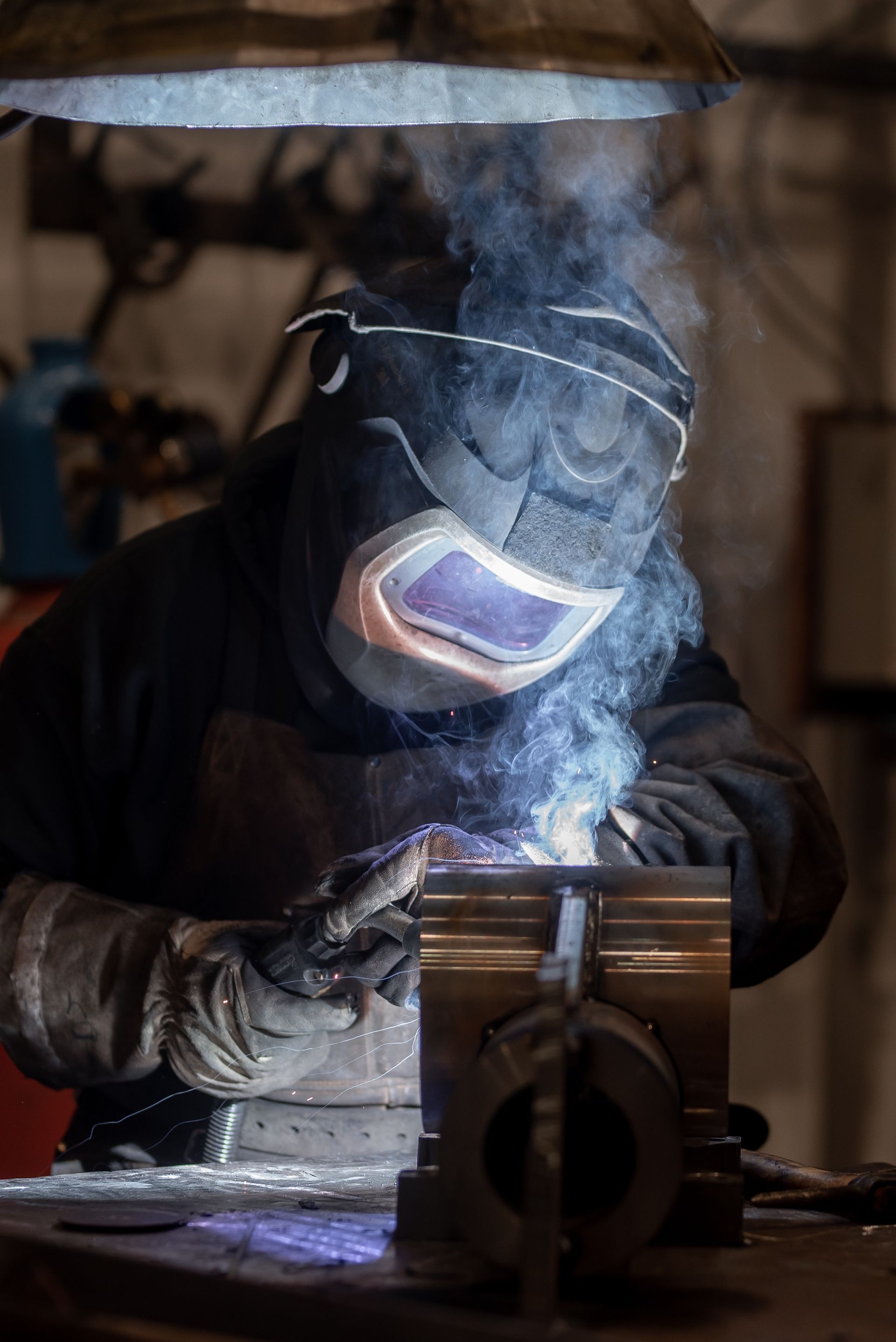 Soudeur dans un atelier sombre, utilisant un chalumeau. Lumière intense, fumée, équipement de protection.
