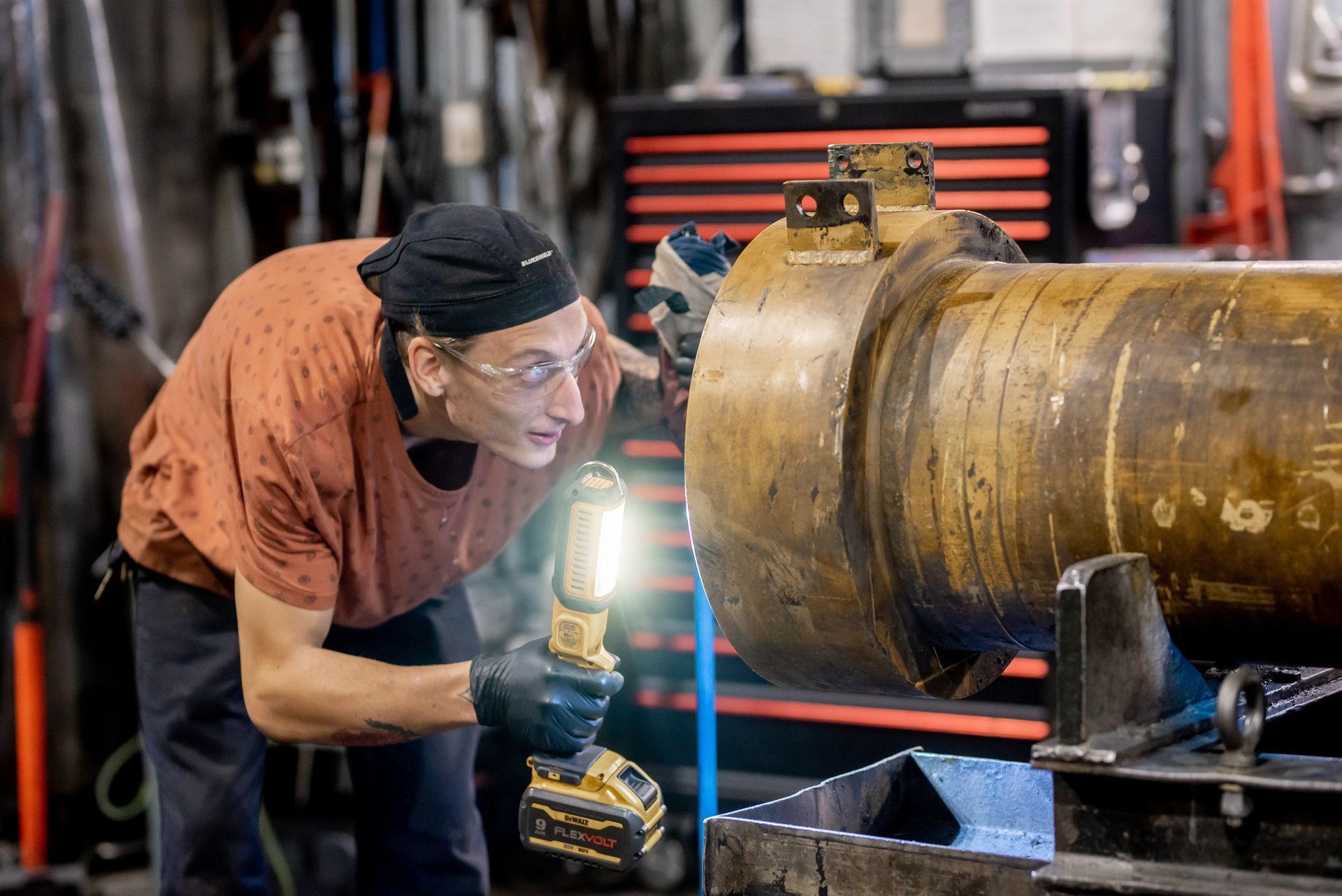 Un homme inspecte un grand cylindre métallique avec une lampe de poche dans un atelier.