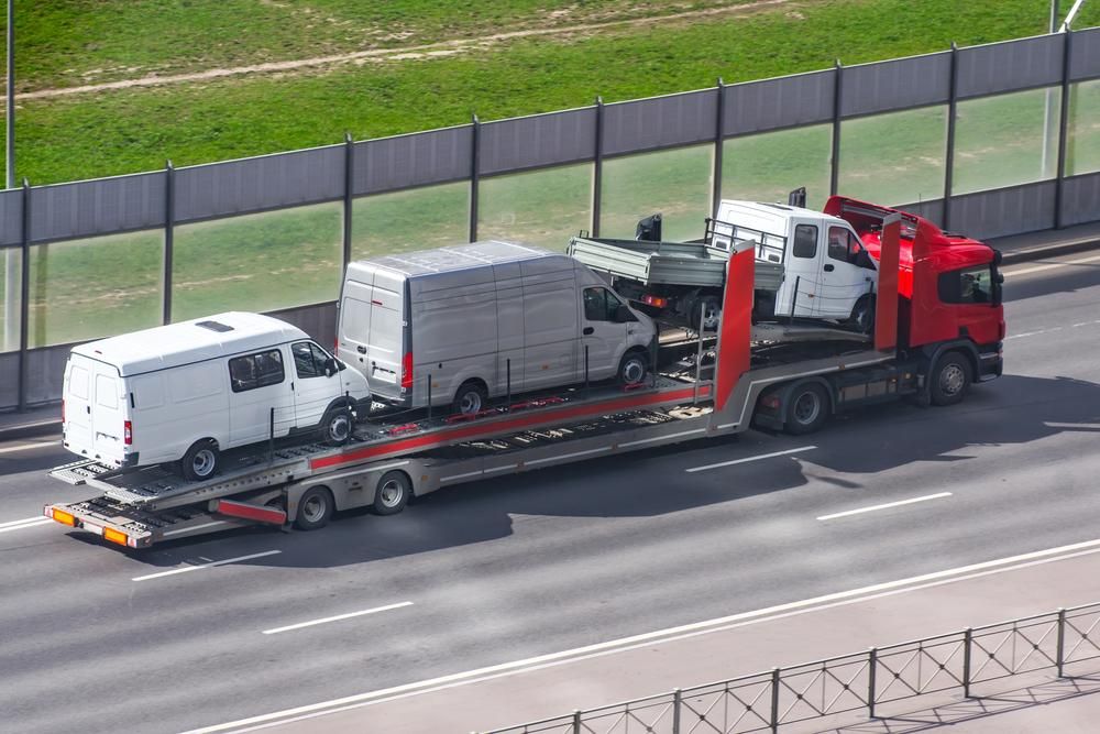 A Truck is Carrying Two Vans on a Trailer on a Highway — DJ's Tilt Tray Service in Coffs Harbour, NSW