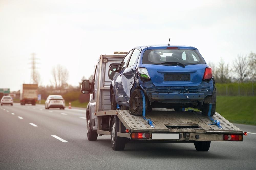 A Tow Truck is Towing a Blue Car on a Highway — DJ's Tilt Tray Service in Woolgoolga, NSW