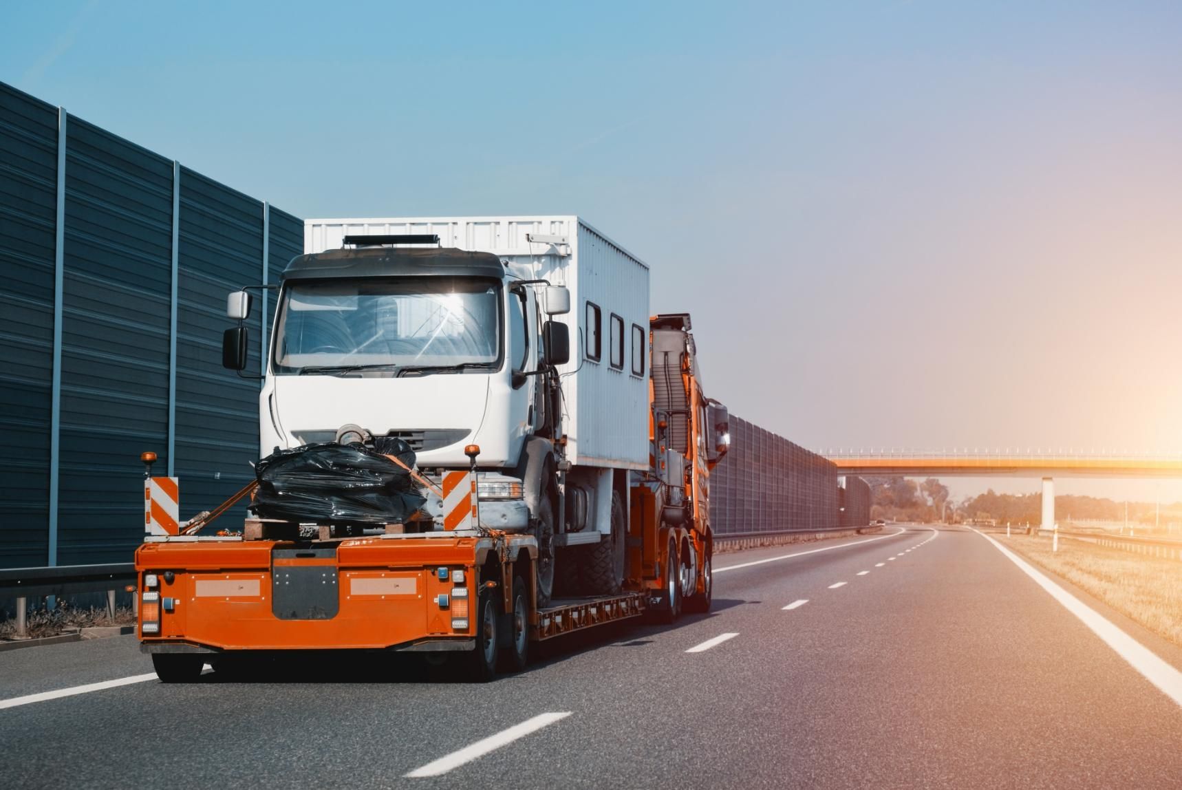 A Truck is Driving Down a Highway With a Trailer Attached to It — DJ's Tilt Tray Service in Urunga, NSW