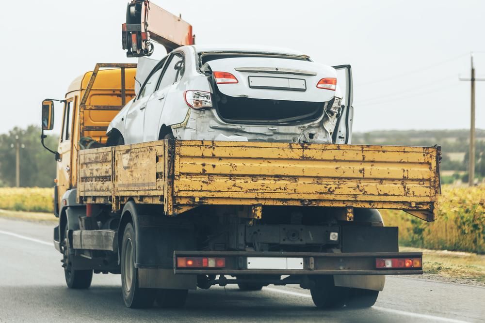 A Tow Truck is Carrying a Damaged Car on the Back of It — DJ's Tilt Tray Service in Coffs Harbour, NSW