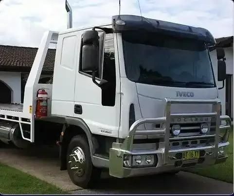 A White Tow Truck is Parked in Front of a House — DJ's Tilt Tray Service in Coffs Harbour, NSW
