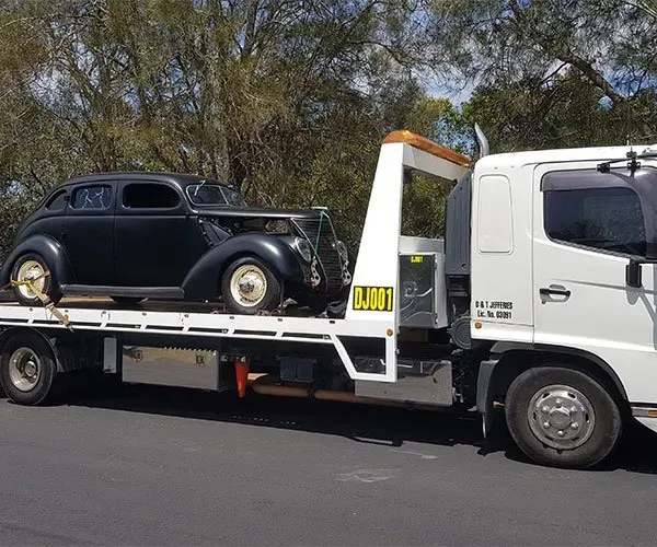 A Black Car is Being Towed by a White Tow Truck — DJ's Tilt Tray Service in Sawtell, NSW