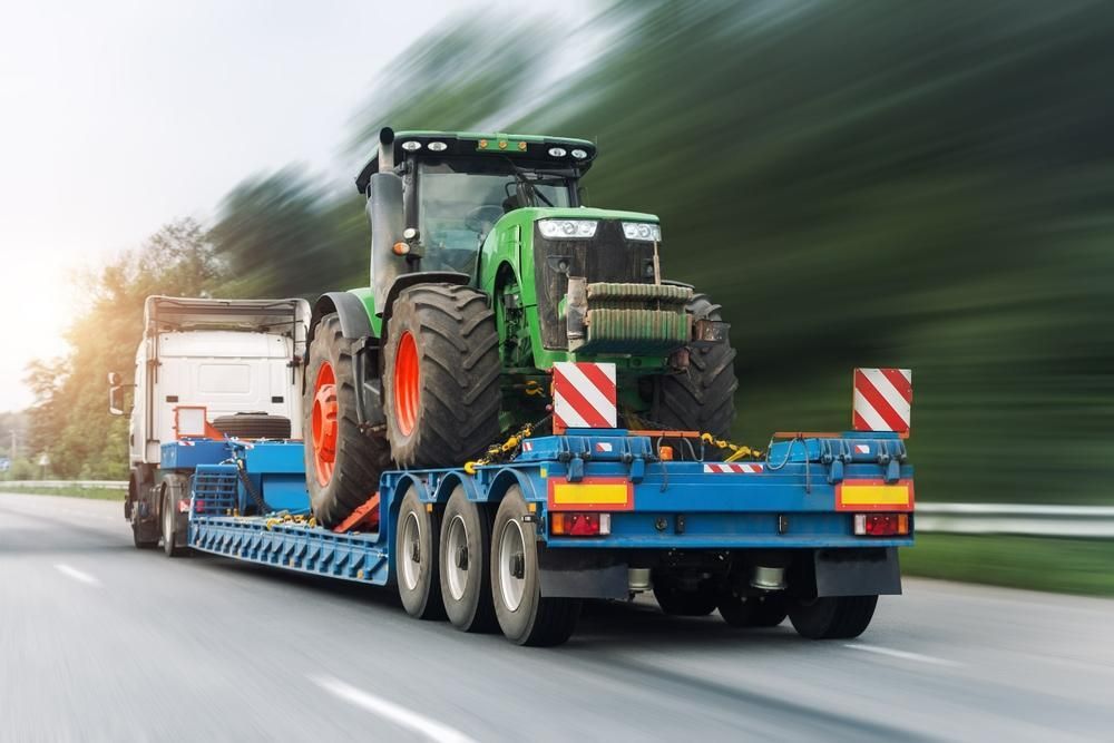 A Tractor is Being Towed by a Semi Truck on a Highway — DJ's Tilt Tray Service in Coffs Harbour, NSW