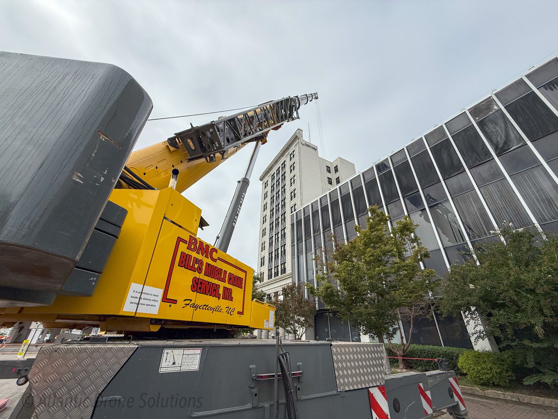 A large yellow crane is sitting in front of a building. — Fayetteville, NC — Bill's Mobile Crane Service