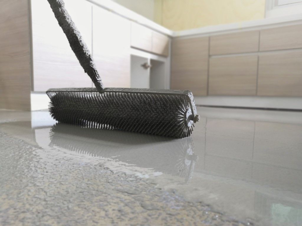 Black paint roller on a shiny floor in a room with white and beige walls.