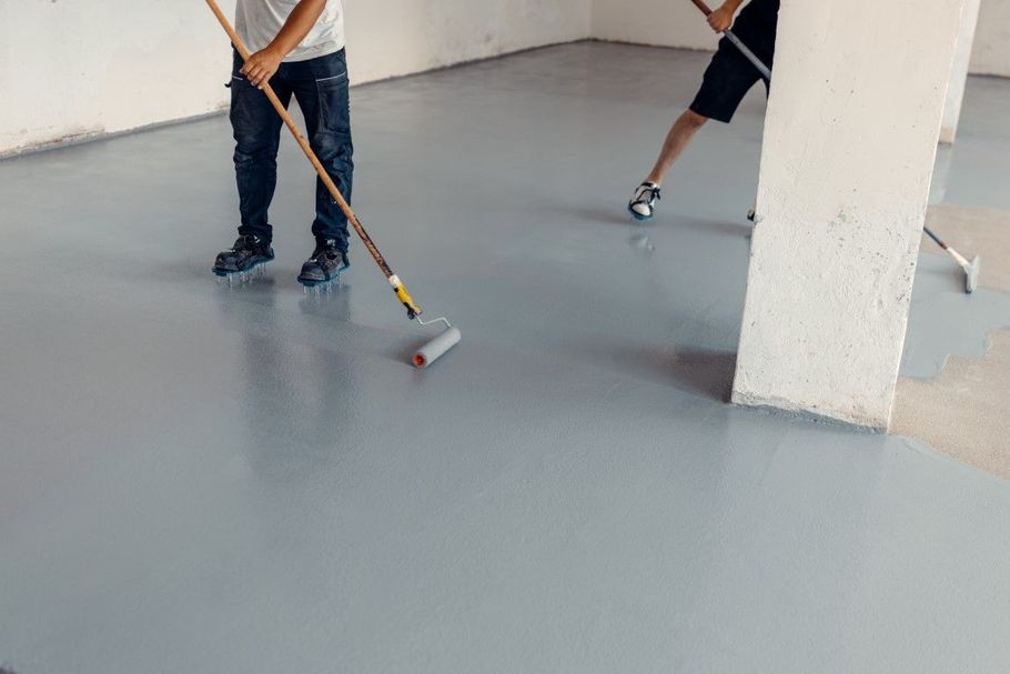 People rolling light blue epoxy onto a concrete floor indoors