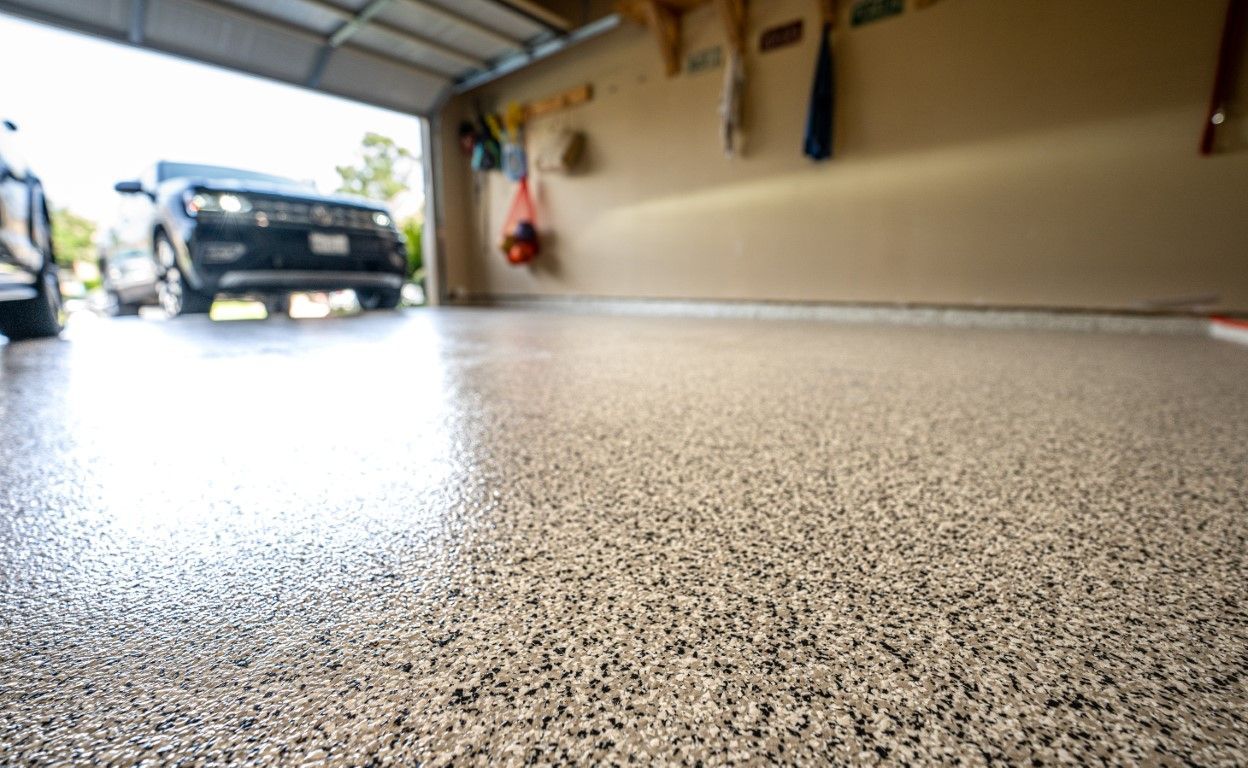 Low-angle view of a speckled garage floor with an open door and a car parked outside