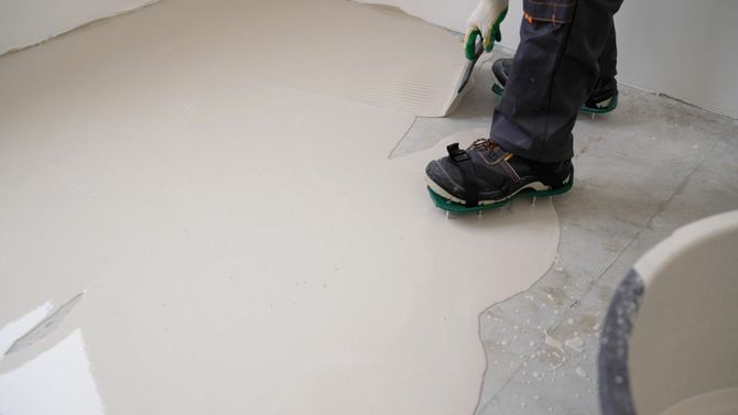 Worker smoothing a light gray floor with a power trowel in a concrete interior