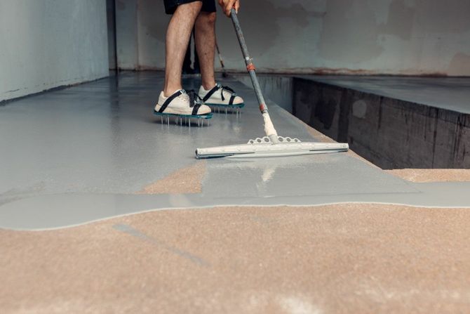 Person mopping a wet concrete floor with tan coating in a gray room