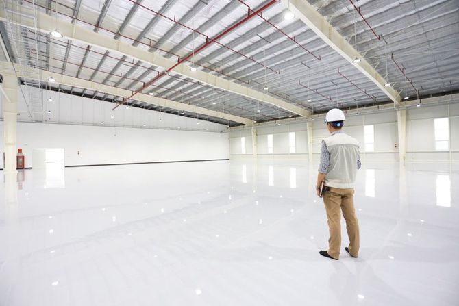 Worker in a hard hat standing in a large empty warehouse with a glossy white floor