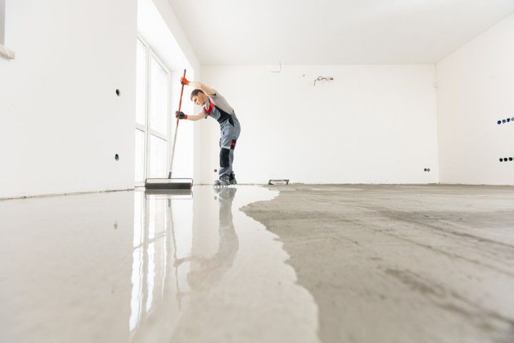 Worker smoothing wet concrete floor in a bright, empty room