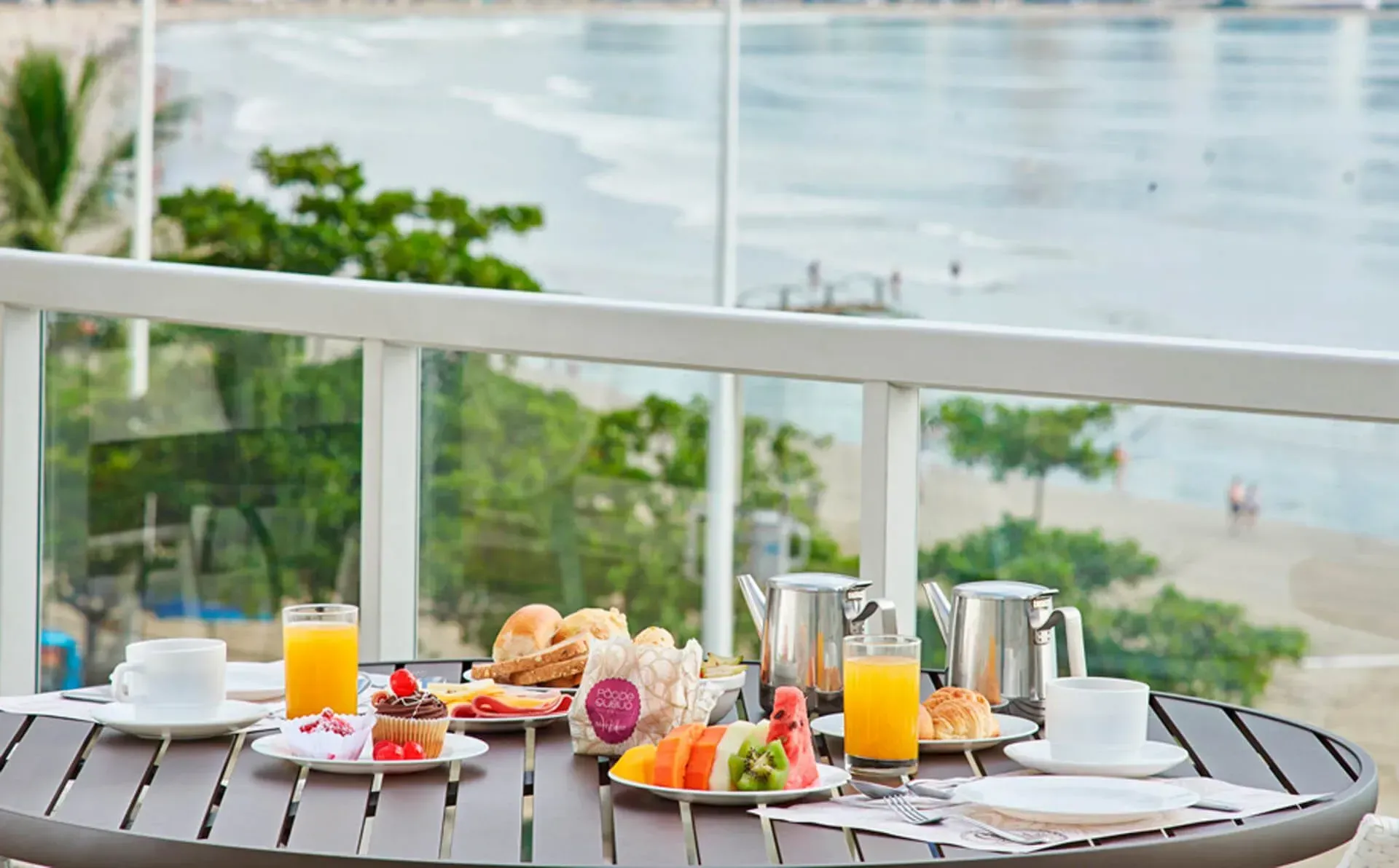 Uma mesa coberta com pratos de comida e bebidas com vista para o oceano.