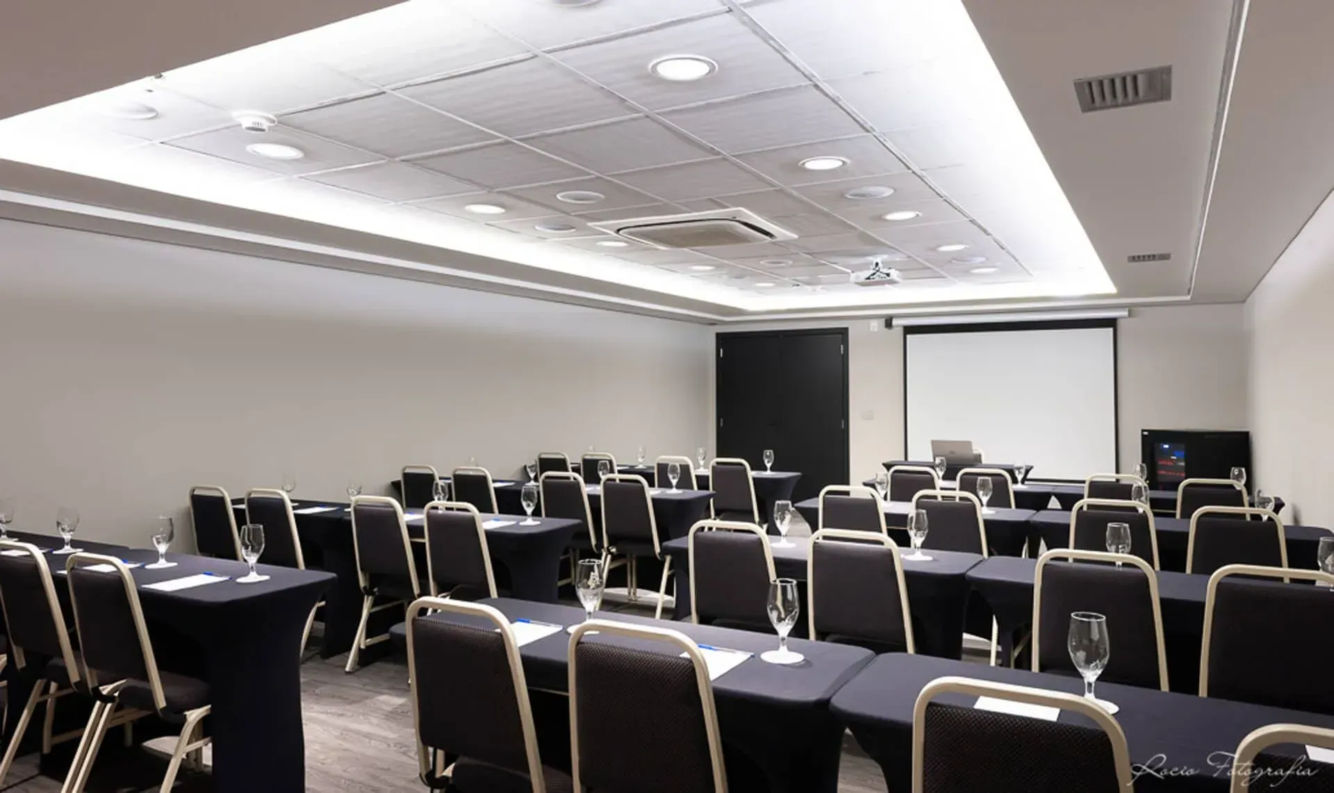 Uma sala de conferências com mesas e cadeiras e uma tela de projetor