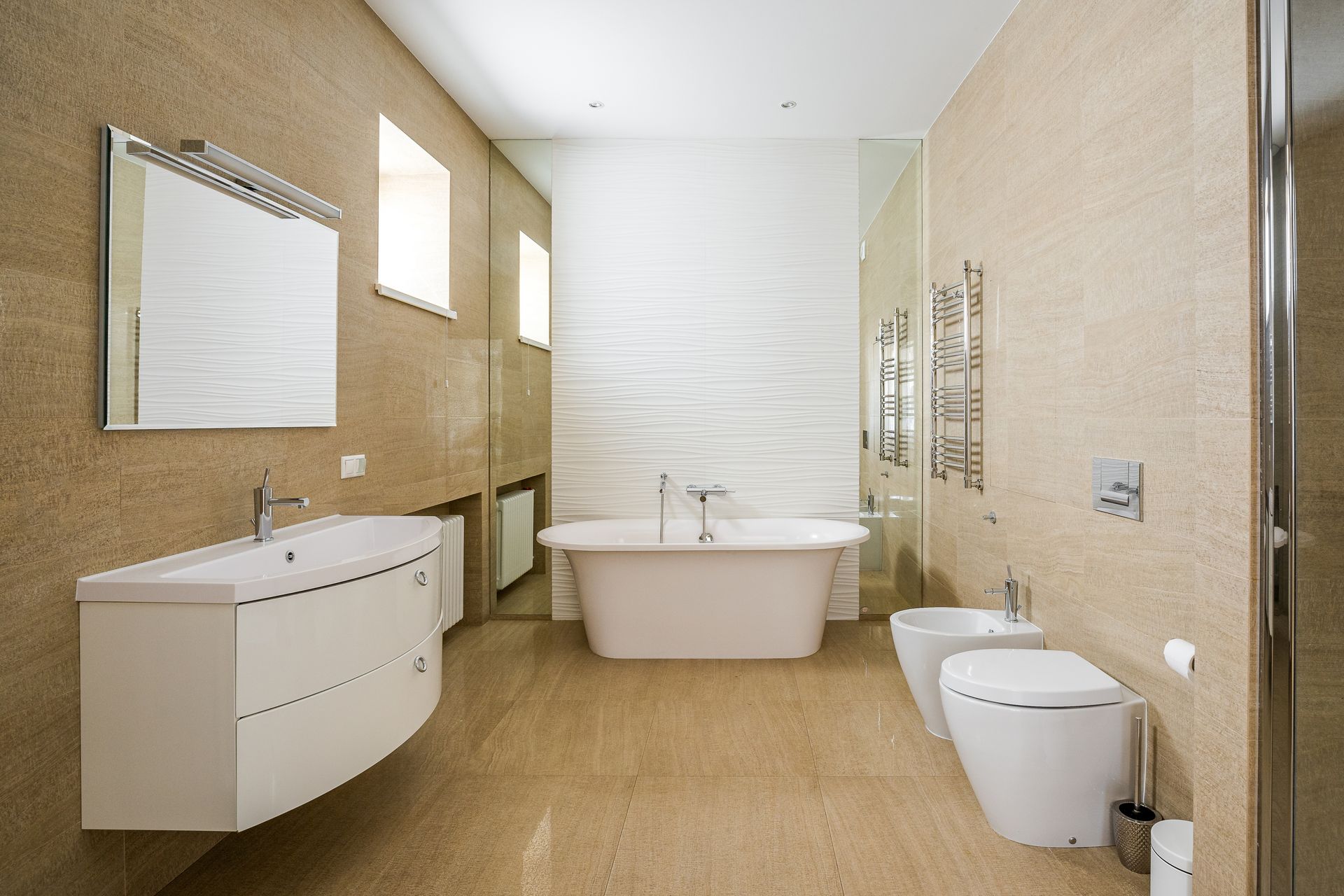 Modern beige bathroom with bathtub, vanity sink, toilet, shower, and wall mirror
