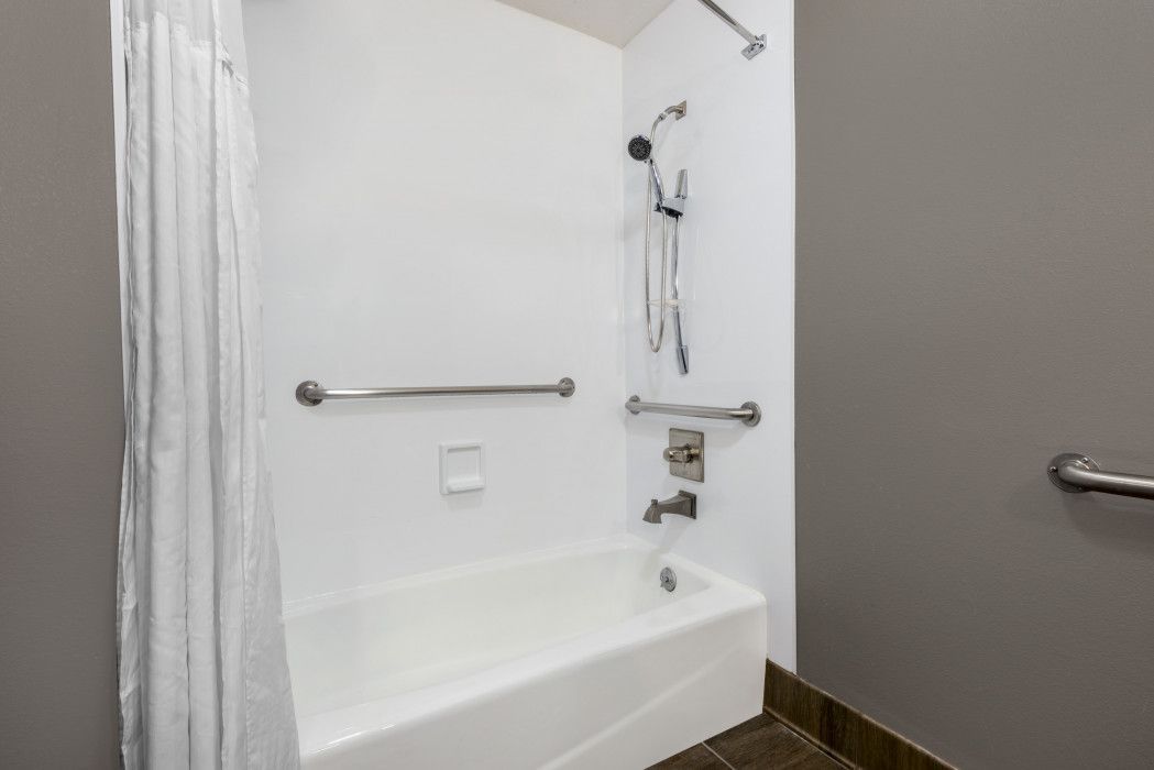 A white bathtub and shower stall with chrome grab bars and a handheld showerhead, set against dark gray walls.