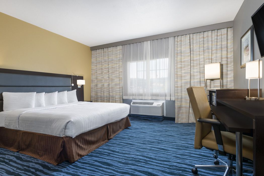 A hotel room featuring a king-size bed with white bedding, a desk with an office chair, and a window with light curtains.