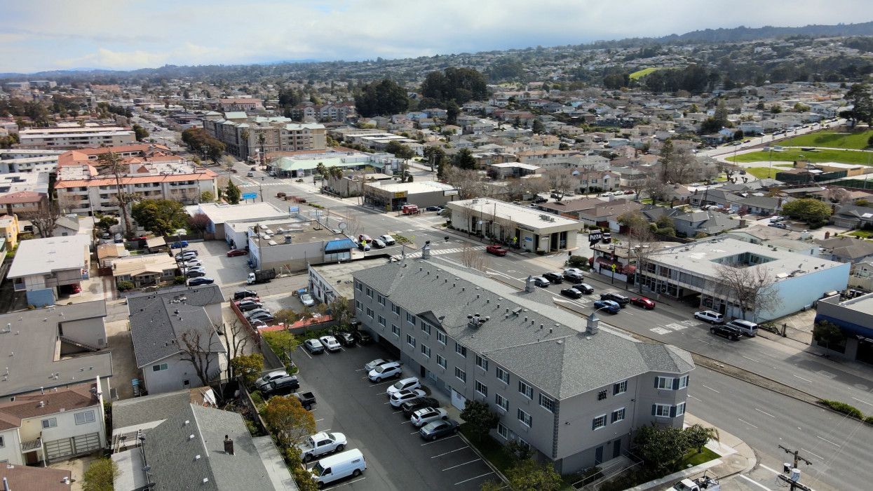 Aerial view of a residential neighborhood with apartment buildings, street-level businesses, and parked cars.