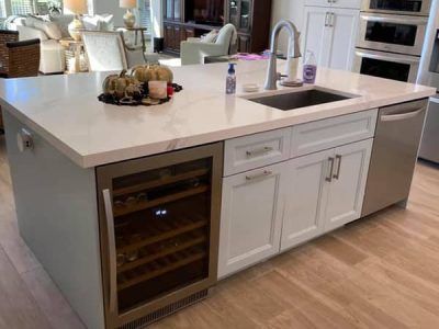 A kitchen with white cabinets , a sink , and a wine cooler.