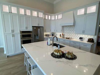 A kitchen with white cabinets , white counter tops , stainless steel appliances and a large island.