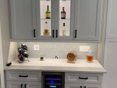 A kitchen with a wine cooler , a wine rack , and a bottle of whiskey on the counter.